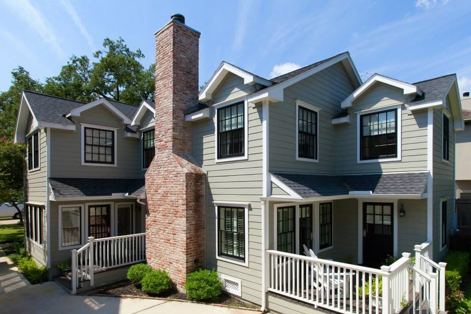 Two-story renovated 1930s home with sage-green siding, white trim, and a restored historic red-brick chimney. Preservation Houston Good Brick Award project.