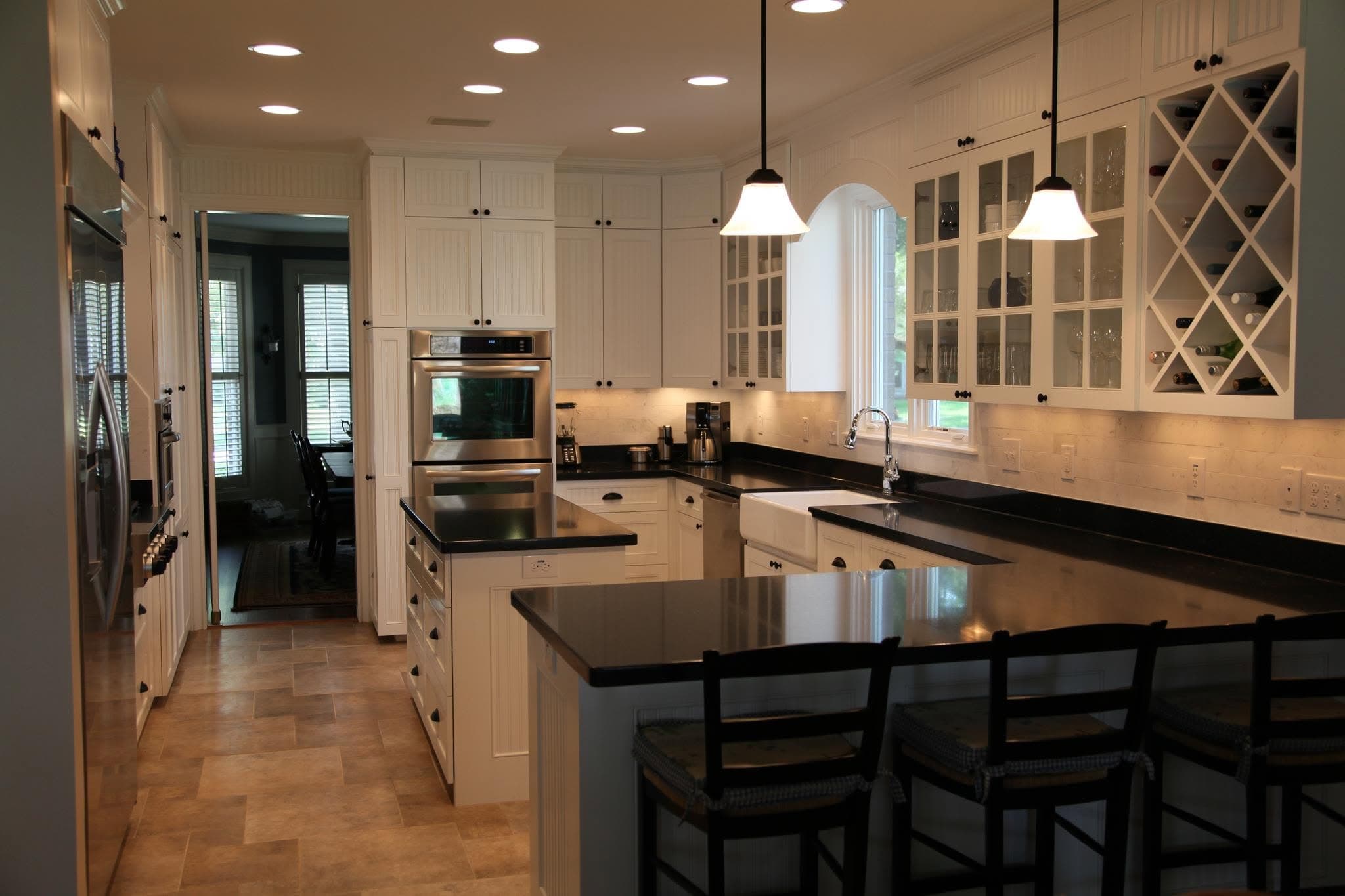 Remodeled kitchen with white cabinets, black granite countertops, farmhouse sink, breakfast bar, and built-in wine rack by Whitley Construction Services.